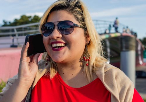 close up portrait young caucasian latin woman smiling talking on the phone outdoors. close up portrait young caucasian latin argentinian woman, plus size model, standing smiling talking on the phone outdoors, at sunset in Buenos aires. smiling happy talking on a call.