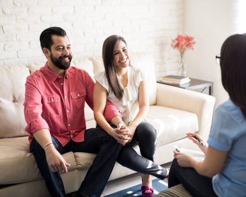 Positive consultation with psychologist Hispanic couple sitting close to each other and holding hands while looking at their therapist